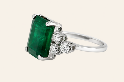A silver ring featuring a large rectangular green emerald-cut gemstone and three small round clear stones on the band, set against a plain white background.