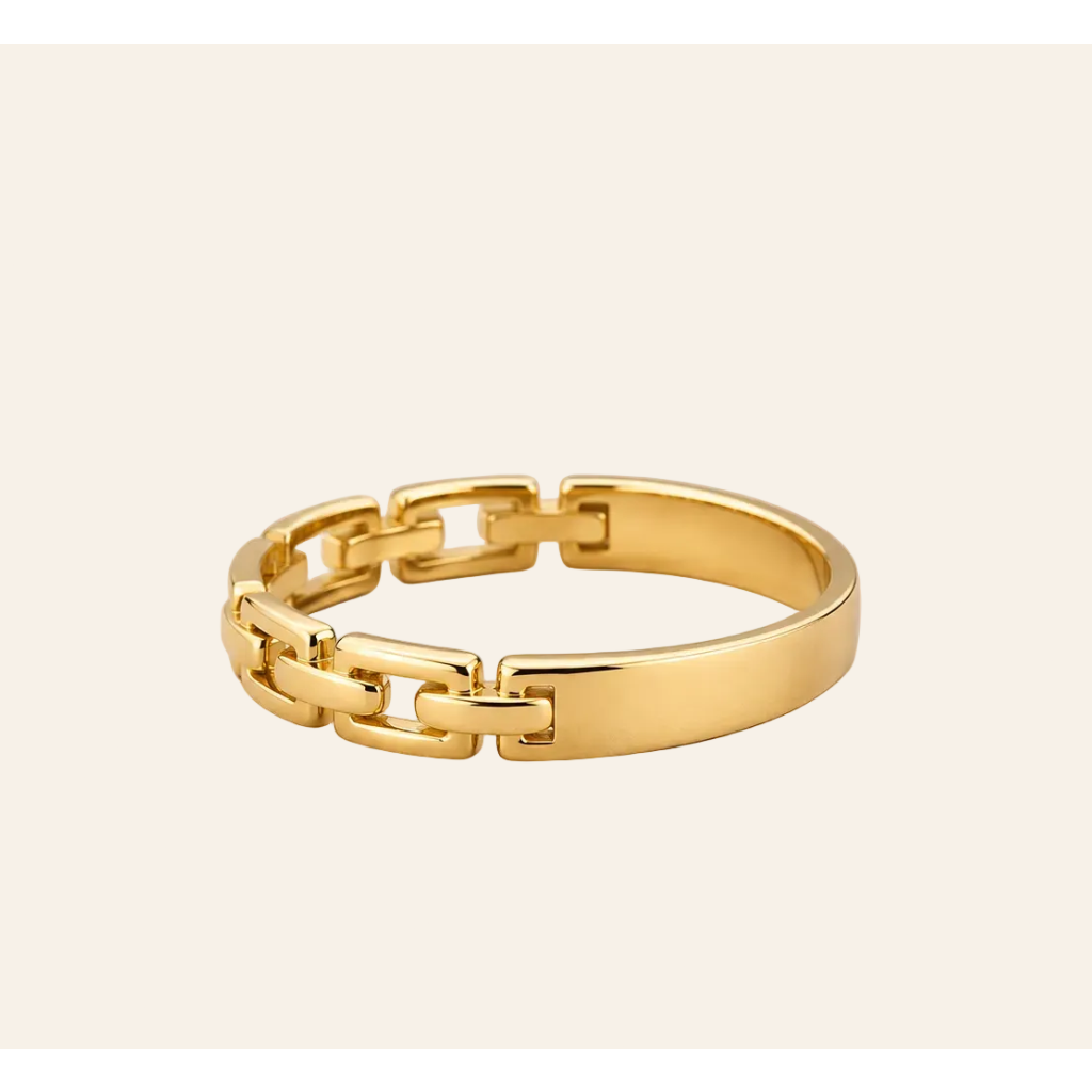 A polished yellow gold ring with a modern chain-link design, photographed on a clean, solid, light beige background.