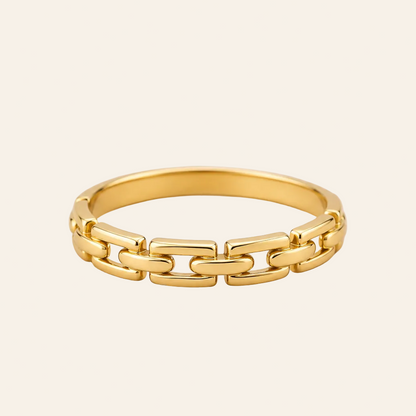 A gold chain-link ring with a polished finish, displayed on a clean, light beige background.